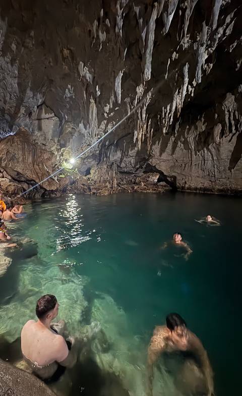 People swimming in a dimly lit natural cave pool.
