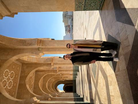 Two people posing under the arches of a monumental structure.