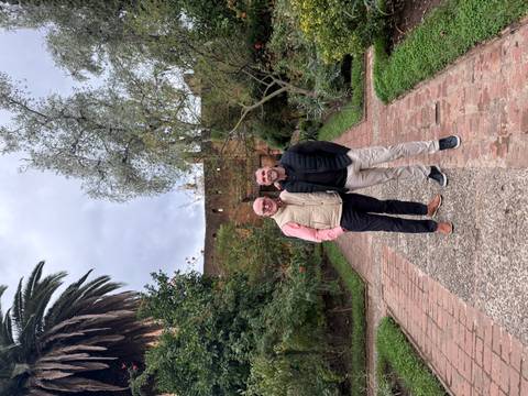       Two men standing in a lush garden area.
  