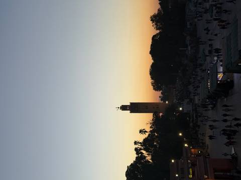       A view of a market square with a minaret and a sunset sky.
  