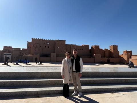       A couple standing in front of a historic structure with a clear sky.
  