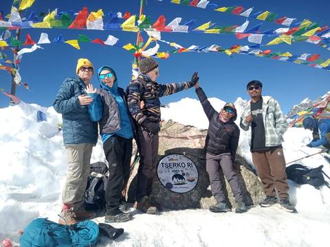 A group of people celebrating at the top of a snowy peak with prayer flags.