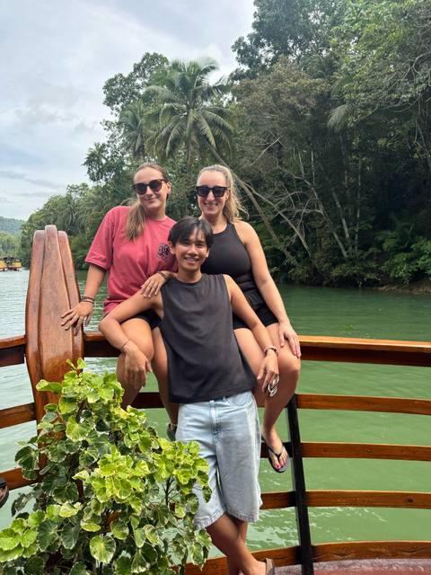 Three people sitting together on a boat in a lush river setting.