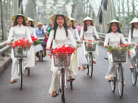 Women in traditional attire riding bicycles on a street.