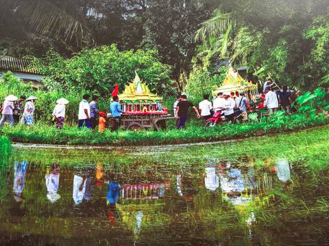 A parade with colorful structures and people walking beside a canal.