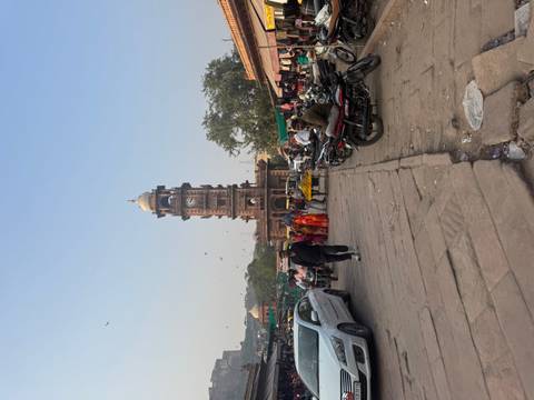 A market street with a clock tower surrounded by people and vehicles.