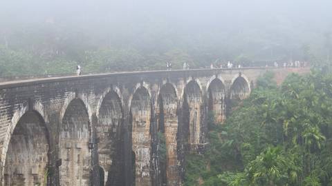       Historic stone bridge covered in mist, with people walking across.
  