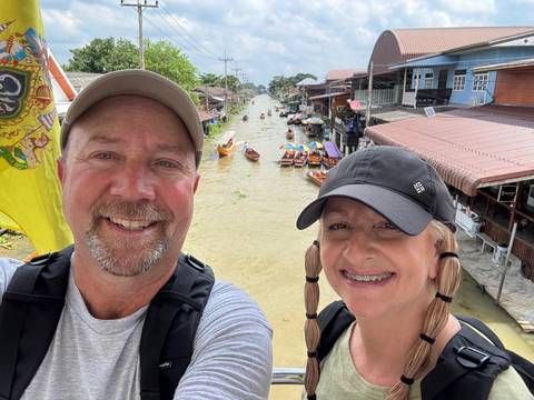 Smiling couple by a canal with boats in the background.