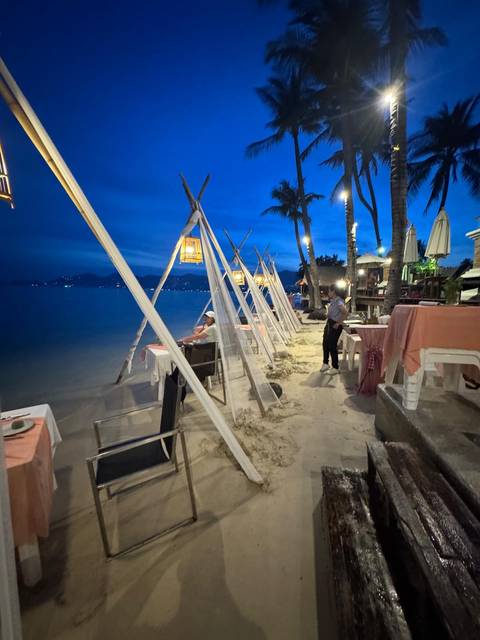 Beachfront dining setup with tables on the sand.