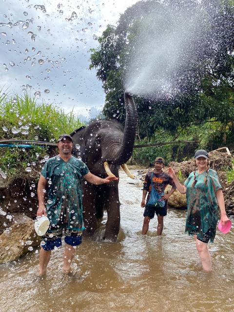       People enjoying a playful interaction with an elephant in a river.
  