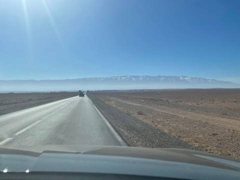       Desert road leading towards snow-capped mountains.
  