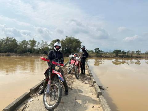 A group of motorcyclists on a narrow path by a water body.