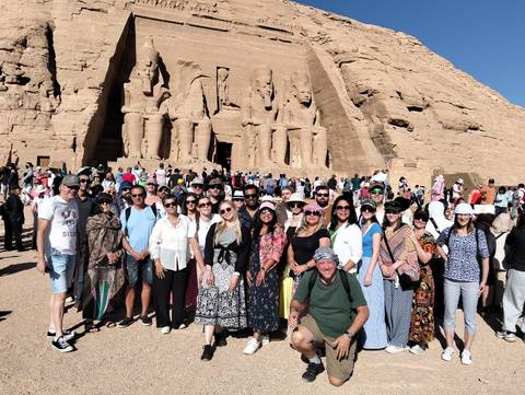 Large group of tourists posing in front of an ancient rock-cut temple.