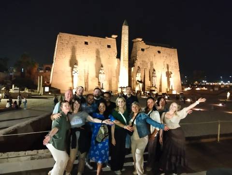 Group of people posing with illuminated ancient Egyptian ruins at night.