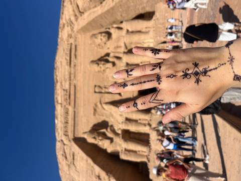 Hand with henna tattoos raised against the backdrop of Abu Simbel.
