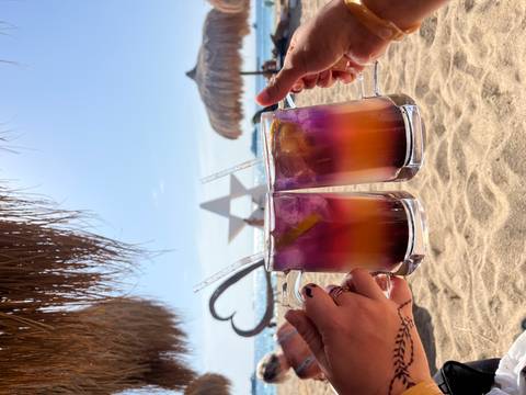 Two colorful cocktails held up against a sandy beach backdrop.