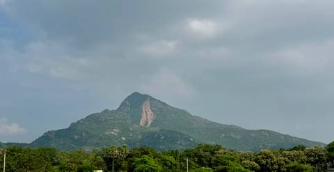 Mountain peak with lush greenery under a cloudy sky.