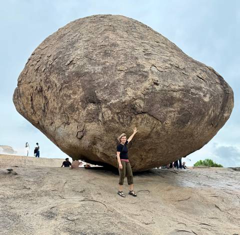 Person posing under a massive balancing rock formation.