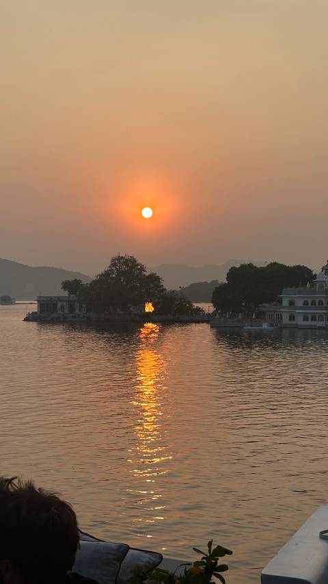 Sunset over a lake with reflections and silhouetted architecture.