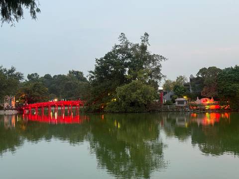 A brightly lit red bridge over a water body with reflections.