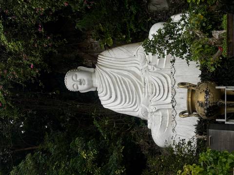A large stone statue of a seated Buddha set amongst greenery.