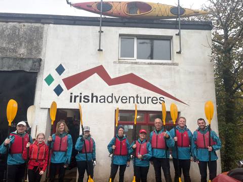 Group of people posing with paddles in front of a building.