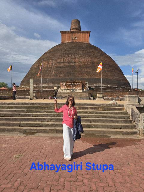 A woman posing in front of a large stupa with flags and stairs.