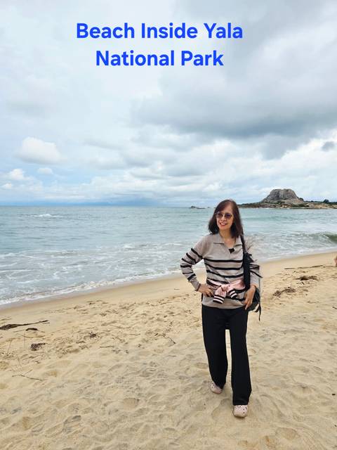A woman standing by the beach with a rocky hill in the distance.