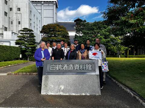 Tour group posing in front of a sake brewery sign.