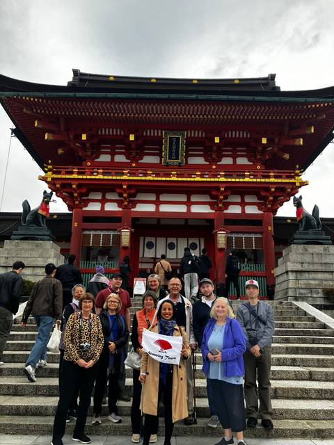 Tourists posing in front of a temple with fox statues.
