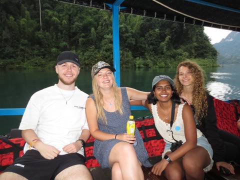 Four people sitting on a boat with a scenic view of a lake and forest in the background.