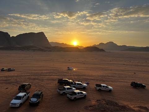 Desert landscape with vehicles and a sunset in the background.