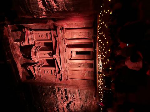       Petra treasury facade lit up at night with an audience seated.
  