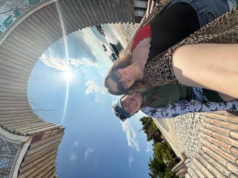       Two women posing on a sandy beach with bright sunshine.
  