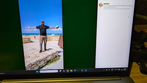 Person posing with arms wide open near the coast, visible on a laptop screen.