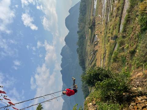 A person on a swing with a scenic view of rice paddies and mountains.