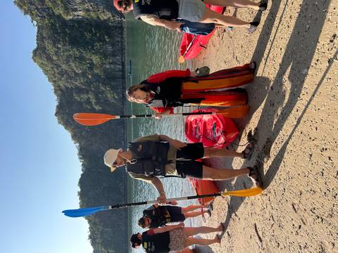 Two people with paddles next to kayaks on a beach.