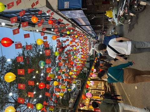 People walking under a street decorated with colorful lanterns and flags.