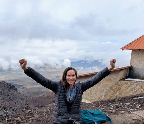       A person raising their arms triumphantly with a mountainous landscape in the background.
  