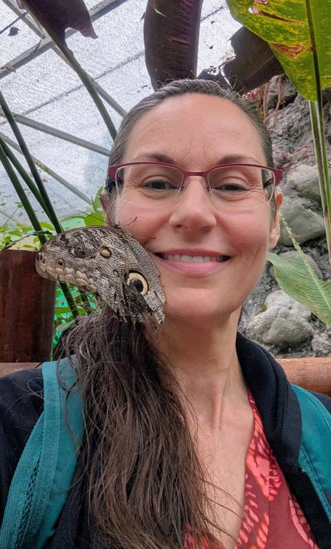       Close-up of a person's face with a butterfly on their shoulder.
  