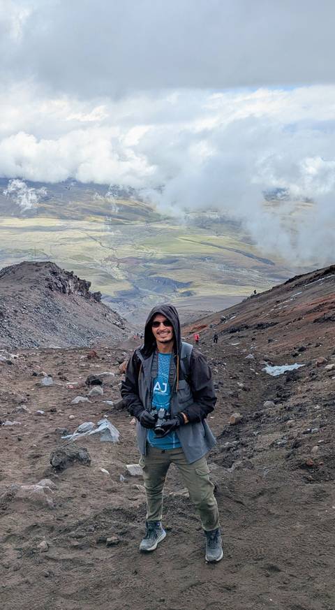       Person standing on a mountainous terrain with scenic valley in the background.
  