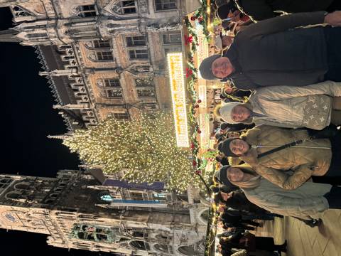       Group at a festive market with a lit Christmas tree at night.
  