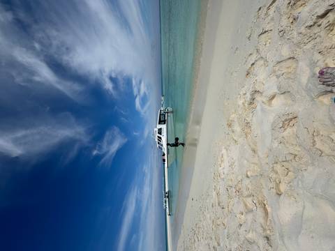       View of a sandy beach with a boat anchored near the shoreline under a blue sky.
  