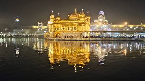 Golden temple reflecting in the calm waters at night.