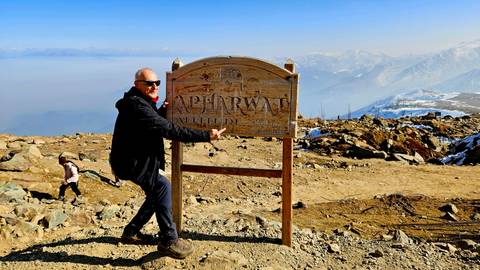 Man posing with a sign on a rocky mountain path.