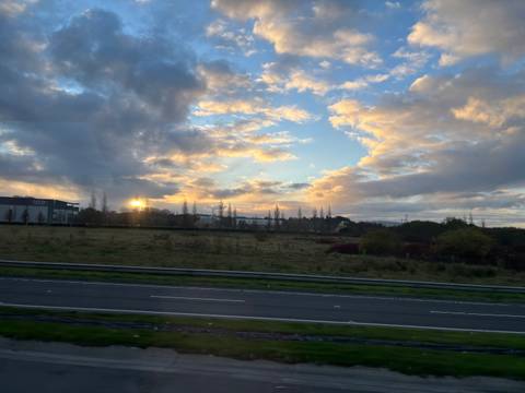 Highway with open field and clouds during sunset.