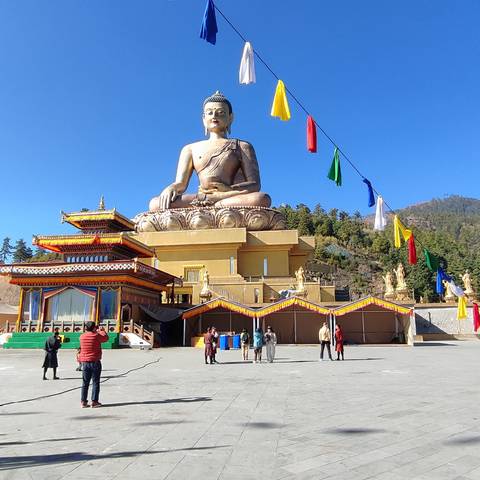 Large seated Buddha statue with visitors in a courtyard.