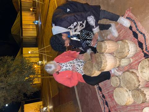 People playing on traditional drums in a camp.