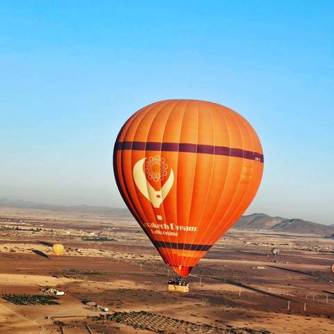 Orange hot air balloon flying over the valley.
