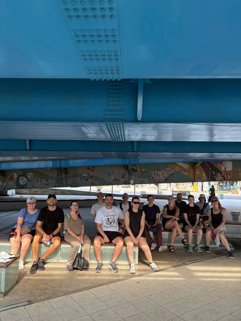 Group of people sitting under a large structure.